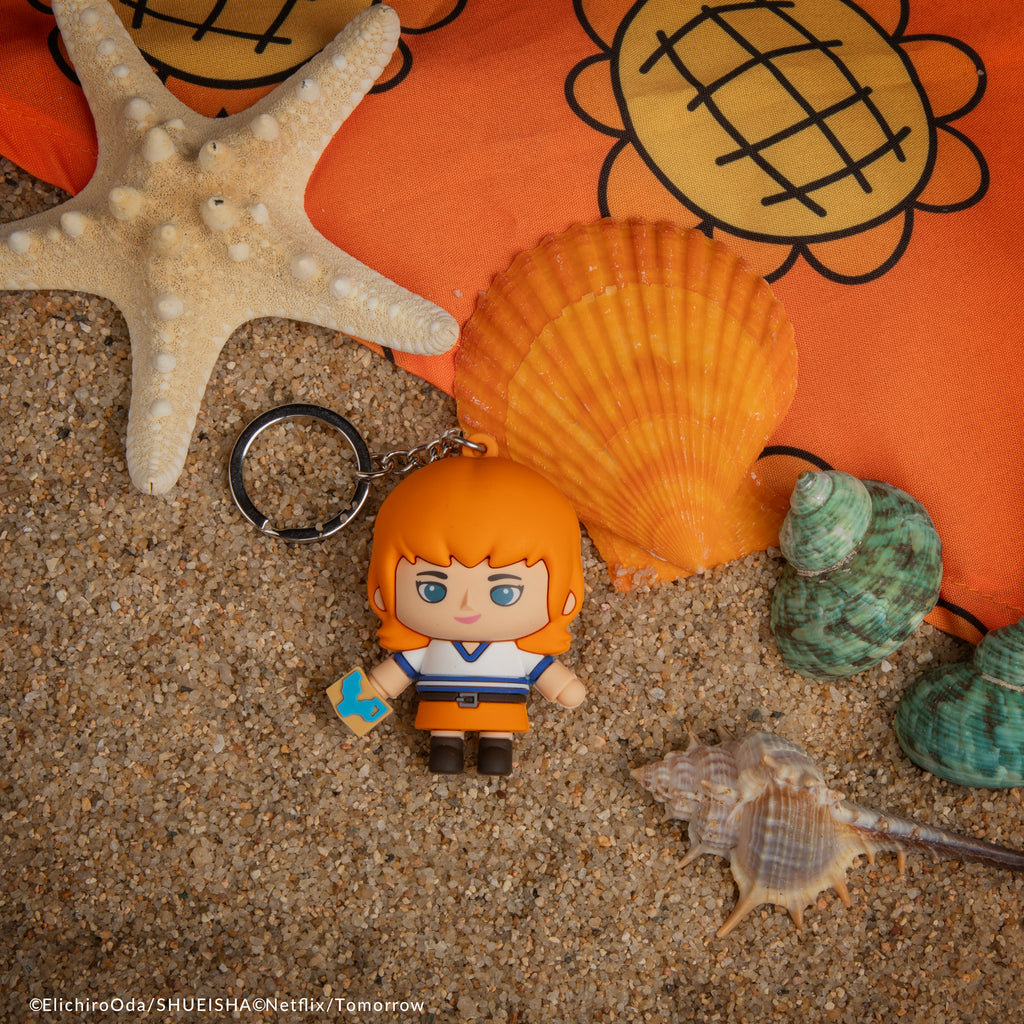 Officially licensed One Piece Nami Gomee Keymate keyring resting on beach sand with sea shells.